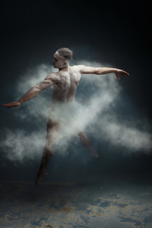 Dancing in flour concept. Muscle fitness guy man male dancer in light blue dust / fog. Guy making dance element in flour cloud. White ribbon as a symbol of lung cancer concept.の写真素材