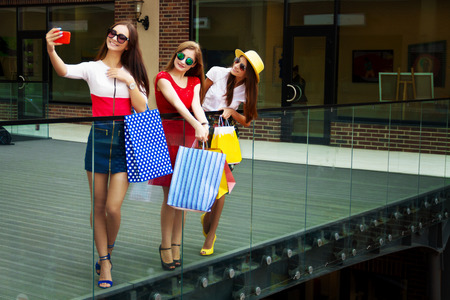 Pretty happy bright women female girls friends in colorful dresses, hats and high heels with shopping bags doing selfie after shopping in shopping mall in summer. Shop sales, black Friday.の写真素材