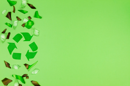 Green and brown cracked shattered glass from bottle lying on green background with green recycle /...
