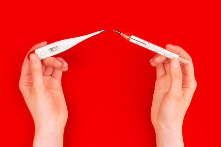 Danger glass human body mercury thermometers compare to safety electric body thermometers on red background. Environment care / issue, recycling / reuse, safe planet, ecology concept.の写真素材