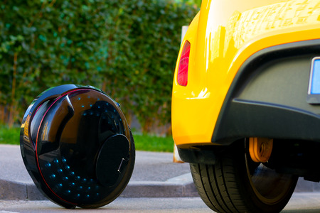 Future is now concept. Ecological transport. Black modern futuristic electric unicycle, unicycle scooter or balancing electric wheel compare with fuel gasoline diesel yellow car. Eco planet conceptの写真素材