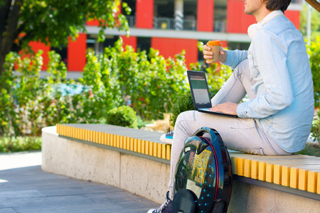 Modern young adult male man student freelancer entrepreneur businessman software engineer with black laptop and futuristic ecological electric unicycle sitting outdoor park working or studyingの写真素材