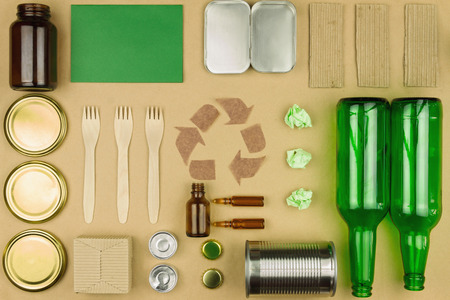 Brown recycle arrow symbol sign with garbage trash: glasses of bottle, wooden disposable tableware, metal cans and jars on craft paper background. Enviromantal issue, ecology care, recycle conceptの写真素材
