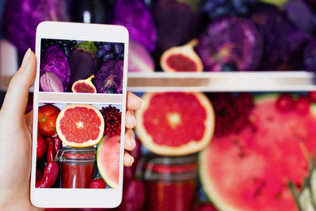 Vegan vegetarian woman female taking picture of healthy antioxidant colorful food, veggies, raw juice and fruits for eating in fridge: grapefruit, tomatoes, watermelon, fig and onion by smartphoneの写真素材