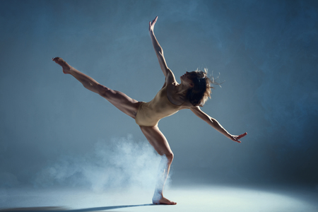 Dancing in cloud concept. Muscle brunette beauty female girl adult woman dancer athlete in fog smoke fume wearing dance bodysuit making stretches dance element performance on isolated grey backgroundの写真素材
