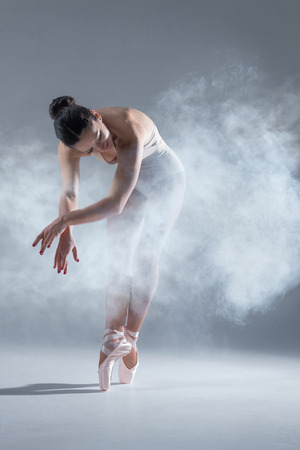 Elegant woman female girl ballerina dancer in beige body pointe shoes dancing, making performance and dance element in fog dust smoke fume on isolated grey background scene. Dancing in cloud conceptの写真素材