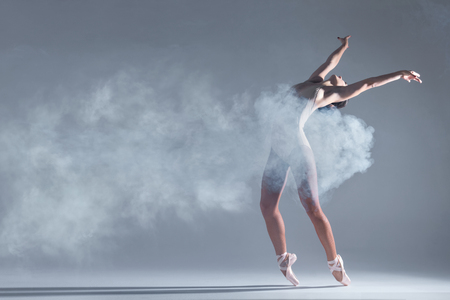 Elegant woman female girl ballerina dancer in beige body pointe shoes dancing, making performance and dance element in fog dust smoke fume on isolated grey background scene. Dancing in cloud conceptの写真素材