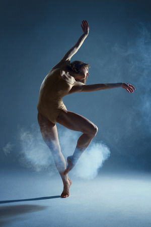 Dancing in cloud concept. Muscle brunette beauty female girl adult woman dancer athlete in fog smoke fume wearing dance bodysuit making emotional dance element performance on isolated grey backgroundの写真素材