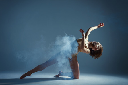 Dancing in cloud concept. Muscle brunette beauty female girl adult woman dancer athlete in fog smoke fume wearing dance bodysuit making emotional dance element performance on isolated grey backgroundの写真素材