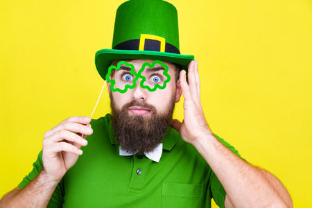 Happy young adult man male in green shirt, green leprechaun hat and tie bow with glasses lucky...