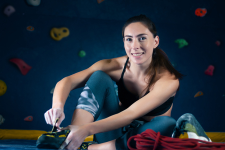 Successful strong self confident sport woman female alpinist climber wears rock climbing shoes before training bouldering on climbing wall. Preparing for complex competition and ready for win concept.の写真素材