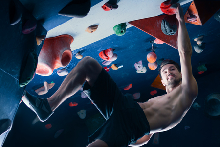 Successful self confident muscle healthy winner climber mountaineer alpinist man male climbing training in climbing wall. Achieved top of wall in bouldering competition. Success and healthy lifestyleの写真素材
