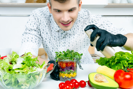Cook chef food stylist men in black gloves prepare decorate splash vegan healthy diet salad in jar with microgreen cherry tomatoes, corn, quinoa, purple cabbage on home kitchen. Food stylist conceptの写真素材