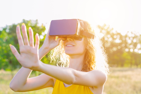 Happy beauty woman female wears summer lite yellow dress smiling and enjoying virtual reality of nature with vr goggles glasses outdoor in park. Active modern futuristic lifestyle leisure concept.の写真素材