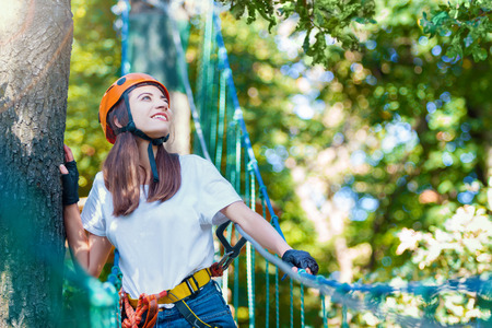 Young beauty female woman adult wears protective helmet having fun in extreme rope park, amusement...