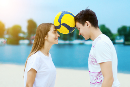 Happy active smiling romantic couple keep the ball heads game on sand beech with blue river lake sky with clouds behind Concept of spring summer outdoor amusement activities entertainment sport trust の写真素材