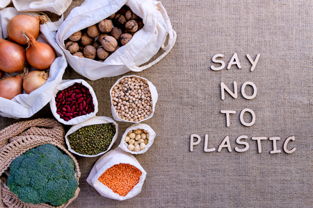Reusable shopping bags on background of burlap. Wooden letters with inscription say no to plastic. Eco pouches with 
chickpeas, hazelnuts, beans, lentils, onions, nuts, broccoli. Zero waste concept.の写真素材