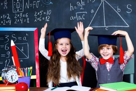 Intelligent smart happy schoolboy and schoolgirl playing in mathematic teacher opposite school chalkboard at school in classroom with school books and notebooks. Back to school, ready to study conceptの写真素材