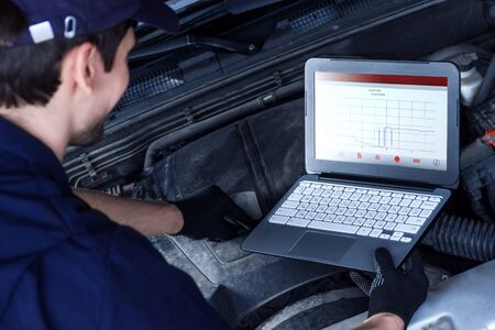 Mechanic is repairing car at service station. Closeup laptop screen with special software at vehicle...