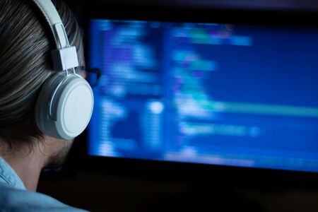Software developer freelancer with white headphones and glasses working with program code: C++,...
