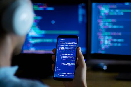 Software developer freelancer with white headphones and glasses working with program code: C++ Java,...