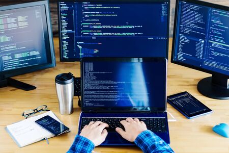 Multiple computer screens with program code on office table. Programmer, developer hands are typing...