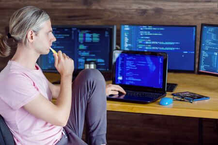 Young man freelancer is working on laptop and brushing teeth at home. Programmer developer dressed...