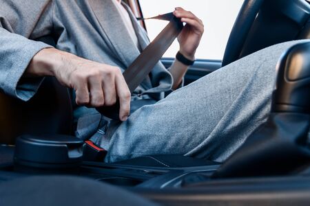 Closeup driver is fastening his seat belt. Young businessman in grey suit is riding behind steering...