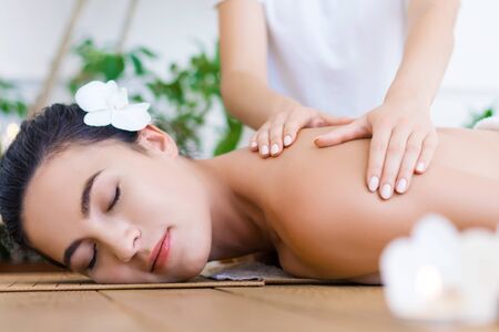Young pleased woman is getting thai massage, therapy. Female hands of master are kneading back of client. Brunette girl is lying on couch in light spa ayurveda salon. Relax and health care concept.の写真素材
