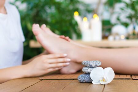 Woman is getting foot massage, therapy. Closeup female hands of master are massaging kneading feet of client. Girl is lying on couch in spa ayurveda salon. Relax and health care concept.の写真素材