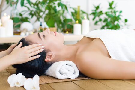 Young pleased woman is getting head massage, therapy. Female hands of master are massaging kneading temples of client. Brunette girl is lying on couch in spa ayurveda salon. Relax and health care.の写真素材