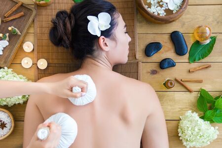 Top view young woman is getting thai massage, therapy. Master hands are massaging client with herbal bags. Brunette girl is lying on couch in light spa ayurveda salon. Relax and health care concept.の写真素材