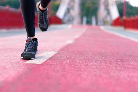 Closeup female legs, in grey sneakers, black leggins, are running on pedestrian urban bridge at city. Woman is doing morning exercises and jogging. Sporty and healthy lifestyle concept.の写真素材