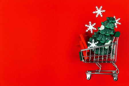 Small green trolley, mini cart filled with shopping bags, packages and christmas tree on red background. Preparing for celebration, buying gifts. Black friday sale. New year fair, market concept. の写真素材