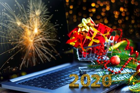 Small green trolley, mini cart filled with bright gift boxes are on laptop computer. Inscription...