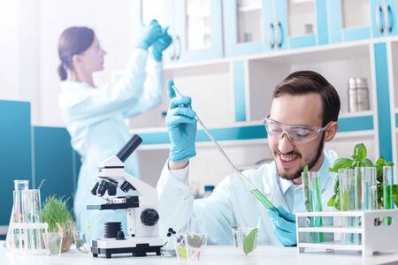 Scientists are working at microbiology laboratory. Man is conducting experiments with plants. Biotechnologist is researching liquid with test tube, pipette and microscope. Biologist workplace. の写真素材