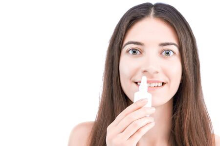 Smiling brunette girl is holding little white bottle with healing drops. Young woman is going to drip medication inside. Cold and flu, runny nose concept. Rhinitis treatment and allergy.の写真素材