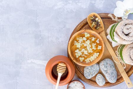 Top view of wooden tray for relaxing healing thai spa treatments. Bowl with flower water, salt, massage grey stones, towel rolls, spices, pot with honey are on cement background. Ayurveda salon.の写真素材