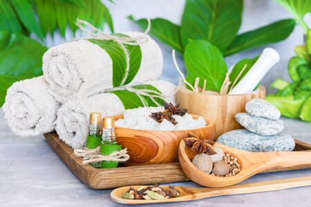 Tray with set for relaxing spa thai treatments. Cotton towel rolls, healing spices, wooden bowl of salt, mortar pounder with herbs, essential oils, stones are on table. Ayurveda salon concept.の写真素材