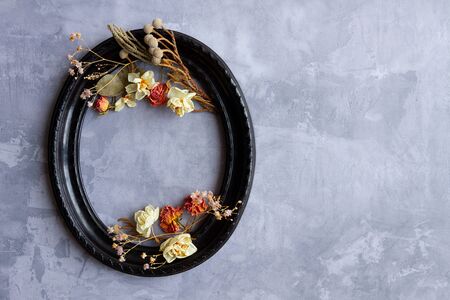 Composition of dried flowers, sprigs, leaves laid out inside black vintage oval frame on concrete cement background. Greeting card template, invitationの写真素材