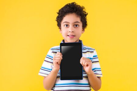 Curly pretty dark skinned boy is holding in hands tablet computer with empty blank screen display....