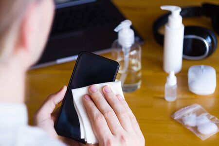 Closeup man is disinfecting smartphone with sanitazer to prevent SARS-CoV-2, 2019-nCoV infection at...
