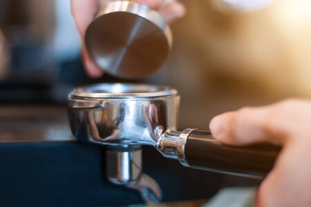Barista woman is preparing, making espresso americano using professional machine, special tool kit in cafe. Closeup female hands are tempering, pressing ground coffee in metal portafilter.  の写真素材