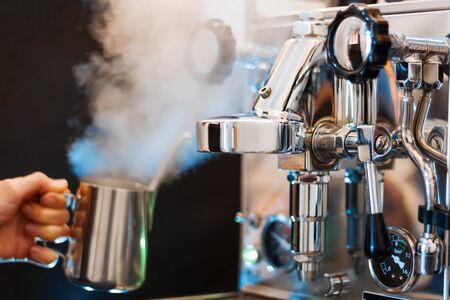 Process of preparing, brewing americano. Closeup female hands are making coffee using professional metal machine in cafe. Barista is heating milk, whipping foam with frother, steam. Hot drinks conceptの写真素材