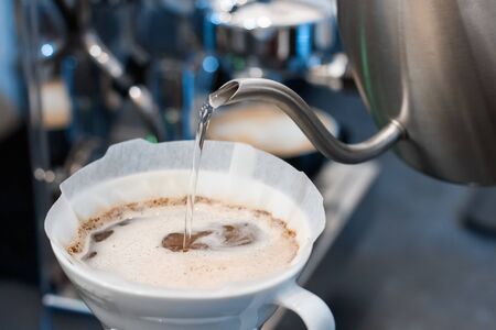 Closeup process of preparing, brewing coffee. Barista is making drink with hand drip method, pouring water on ground with filter, using special set of kettle and glass capacity. Hot beverages concept.の写真素材