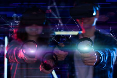 Closeup hands are holding wireless controllers. Boy and girl are playing in virtual reality game...