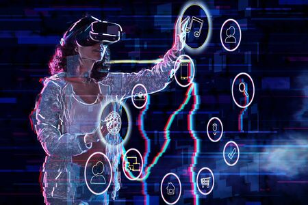 Teenage curly girl is playing in virtual reality game club. Smiling young woman in VR glasses is...