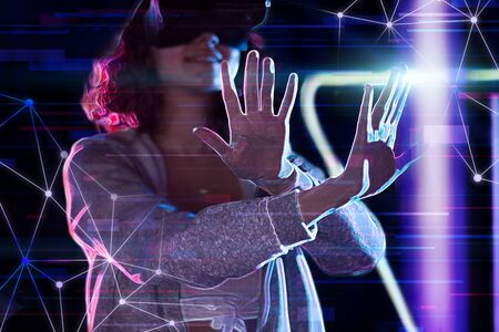 Teenage curly girl is playing in virtual reality game club. Smiling young woman in VR glasses is...