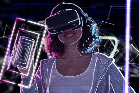 Teenage curly girl is playing in virtual reality game club. Smiling young woman in VR glasses is...