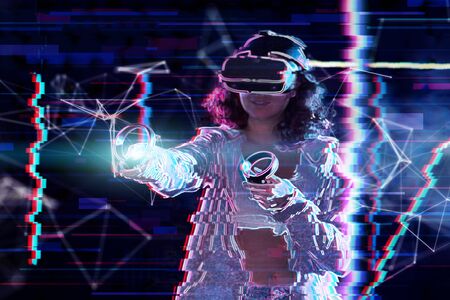 Teenage curly girl is playing in virtual reality game club. Smiling young woman in VR glasses is...